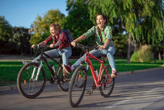 Two pretty young caucasian girls having fun on bicycles along the street. Best friends enjoying a day on bikes. Sunny summer evening.