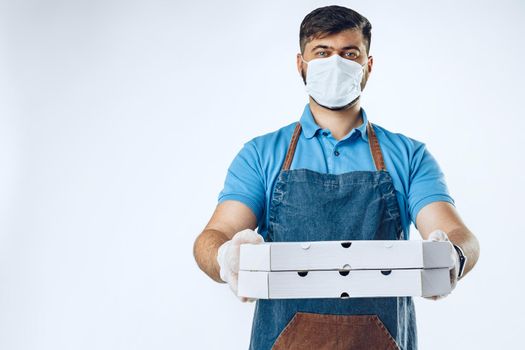 Pizza delivery man in medical gloves and mask against grey background. Safe service while coronavirus covid-19 outbreak