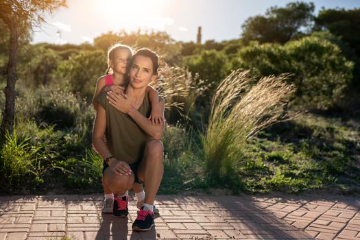 Beautiful mother and her little daughter outdoors. Beauty Mum and her Child sitting on Park pathway together at sunset. Outdoor Portrait of happy family. Mother's Day.