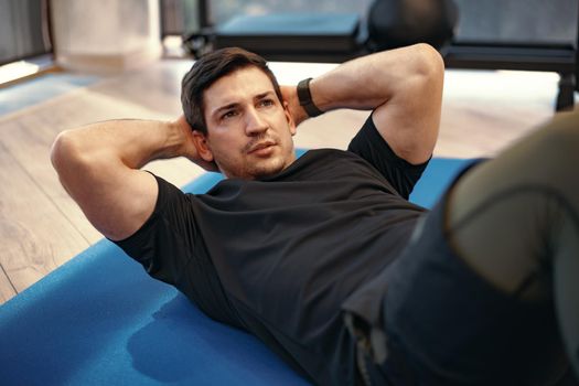 Young muscular caucasian handsome man doing abs exercises on a mat