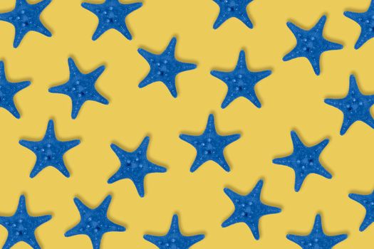 Dried toned in blue sea star fish pattern on yellow background. Top view, flat lay.