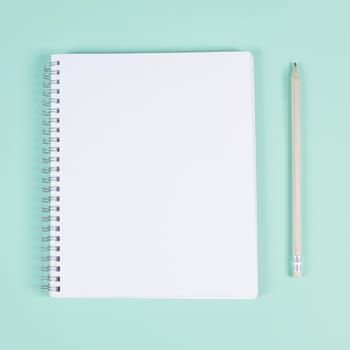 blank spiral notebook with pencil turquoise background