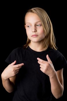 Pretty girl pointing at herself with her hands. Portrait of beautiful blonde teenage girl in black t-shirt gesturing against black background.