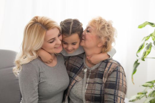 Portrait of three generations of women look at camera posing for family picture, cute little girl hug mom and granny enjoy time at home, smiling mother, daughter and grandmother spend weekend together