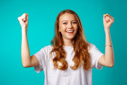 Happy cheerful excited young woman celebrating her success against blue background