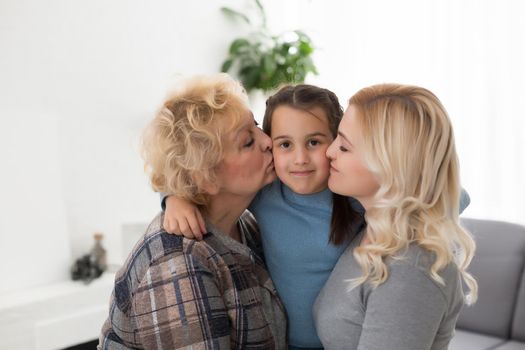 Three generations of women. Beautiful woman and teenage girl are kissing their granny while sitting on couch at home