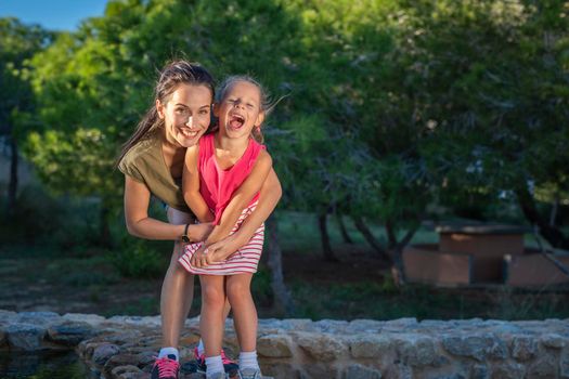 Beautiful mother and her little daughter outdoors. Beauty Mum and her Child playing in Park together at sunset. Outdoor Portrait of happy family. Mother's Day.