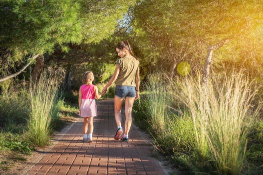 Beautiful mother and her little daughter outdoors. Beauty Mum and her Child walking in Park together at sunset. Outdoor Portrait of happy family. Mother's Day.