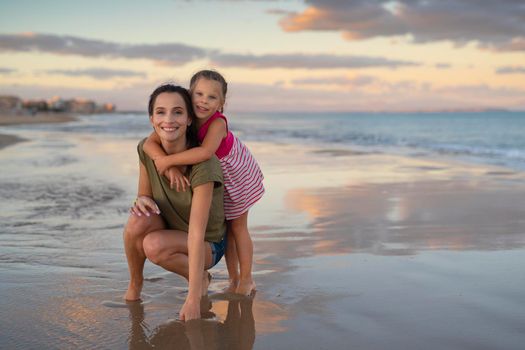 Happy family. Young happy beautiful mother and her daughter having fun on the beach at sunset. Positive human emotions, feelings.