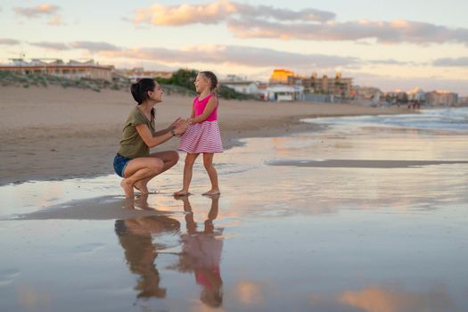 Happy family. Young happy beautiful mother and her daughter having fun on the beach at sunset. Positive human emotions, feelings.