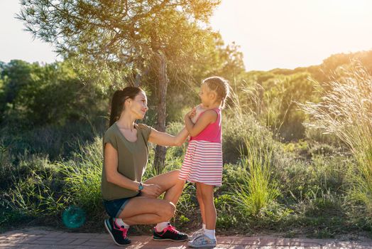 Beautiful mother and her little daughter outdoors. Beauty Mum and her Child sitting on Park pathway together at sunset. Outdoor Portrait of happy family. Mother's Day.