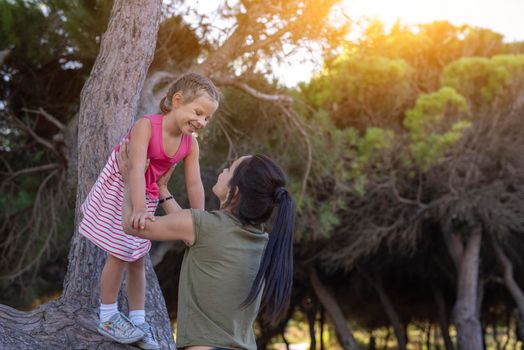 Beautiful mother and her little daughter outdoors. Beauty Mum and her Child playing in Park together at sunset. Outdoor Portrait of happy family. Mother's Day.