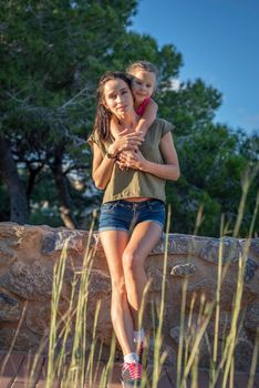 Beautiful mother and her little daughter outdoors. Beauty Mum and her Child posing in Park together at sunset. Outdoor Portrait of happy family. Mother's Day.