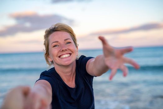 Follow me - happy young woman pulling guy's hand - reaching out she`s friend at sunset seaside - concept of carefree modern life.