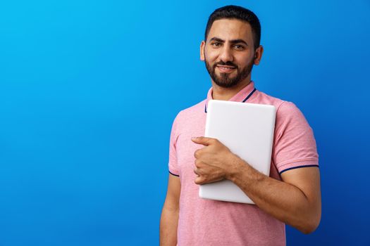 Portrait of positive man standing and holding laptop against blue background, close up