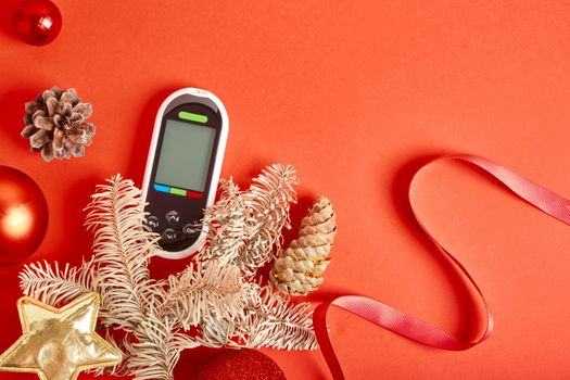 glucose meter christmas and new year decorations, diabetes and holidays concept, glucometer as a gift, red background copy space top view