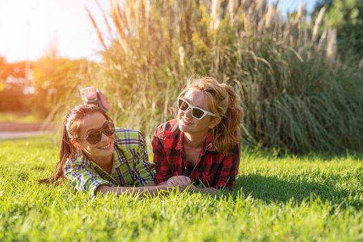 two young pretty teenager girls best friends laying on grass at sunny summer day.
