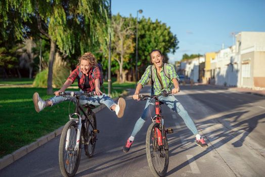 Two pretty young caucasian girls having fun on bicycles along the street. Best friends enjoying a day on bikes. Sunny summer evening.