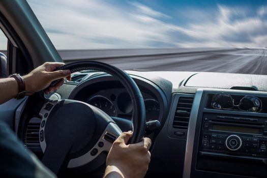 Hands of a driver on steering wheel of a car and empty asphalt road