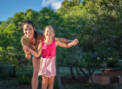 Beautiful mother and her little daughter outdoors. Beauty Mum and her Child playing in Park together at sunset. Outdoor Portrait of happy family. Mother's Day.