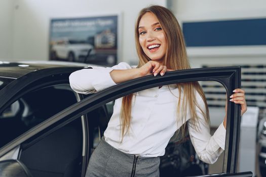 Beautiful young woman touching her new car with pleasure and joy