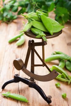 Fresh green peas on vintage scales on old wooden background. Selective focus. Healthy food concept.