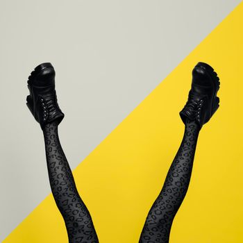 New gray female boots on long slender woman legs in gray tights isolated on yellow and gray background. Pop art concept with Heavy Duty Boots.