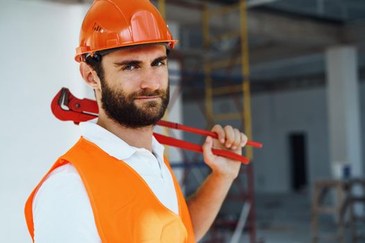 Young male plumber in workwear holding pipe wrench on a construction site indoors