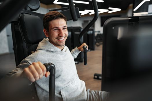 Young fit bodybuilder man doing arms workout training in the gym on machine, close up