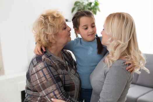 Three generations of women. Beautiful woman and teenage girl are kissing their granny while sitting on couch at home