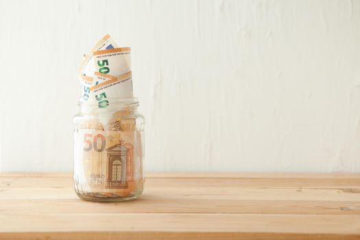 euro money banknotes in the glass jar at wooden table. Business concept. Money cash savings in glass pot at home.