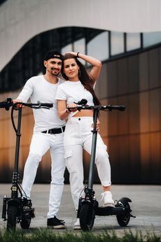 A girl and a guy are walking on electric scooters around the city, a couple in love on scooters