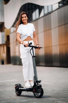 beautiful girl in white stylish clothes on an electric scooter in the city.