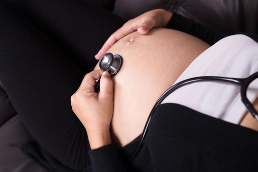 close up pregnant woman listening baby's heartbeat with stethoscope placed on her belly