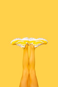 New Yellow female sneakers on long woman legs in yellow tights isolated on yellow background. Monochrome pop art concept. Vertical banner with copy space