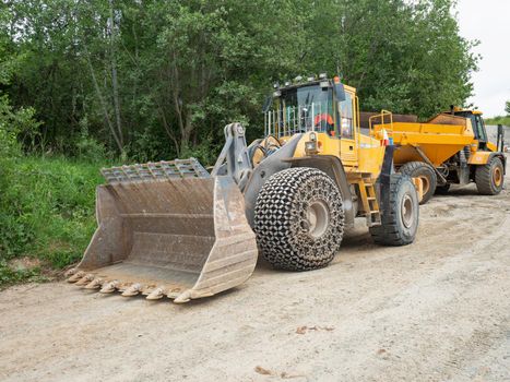 Heavy loader bulldozer bucket. Tractor loader with protective wheel chains on tyres waits at the sandpit 