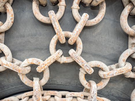 Wheel chains with sandy dirt on huge tire of construction or quarry machine. Chains with ring chain links closeup. Grungy rough chains 