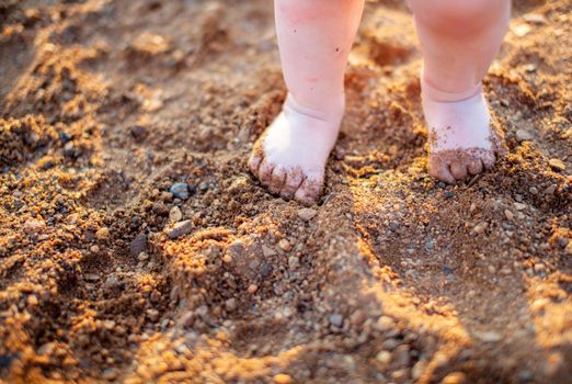 Children's bare feet in summer on a golden sandy beach close-up. The concept of child safety. The concept of recreation with children.