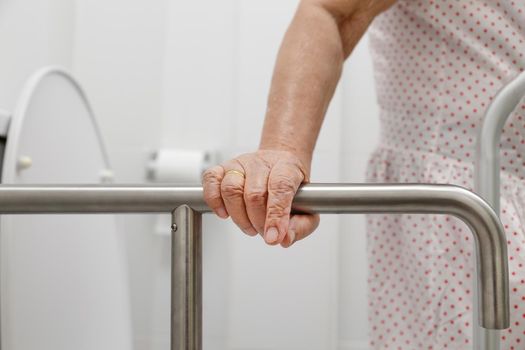 Elderly woman holding on handrail in toilet.