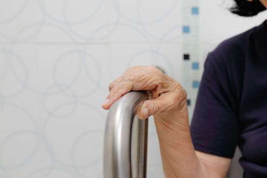 Elderly woman holding on handrail in bathroom.