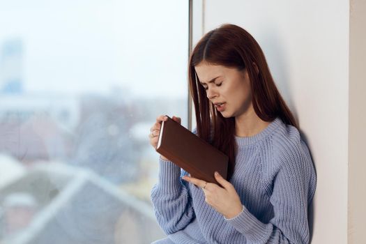 woman reading a book near the window with a cup of drink rest. High quality photo