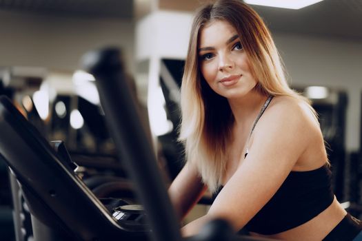 Fit curvy young blonde woman training in a cardio zone in a gym close up