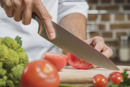 chef s male hand cutting tomato with sharp knife board