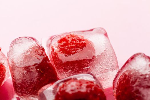 Raspberry ice cubes on pink glossy background. Close up.