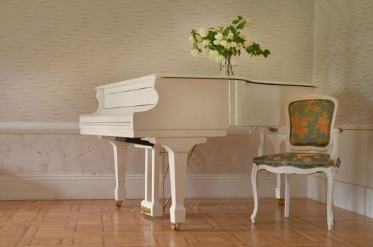 white grand piano standing in elegant white interior of palace hall. white piano at the empty reto room with chair