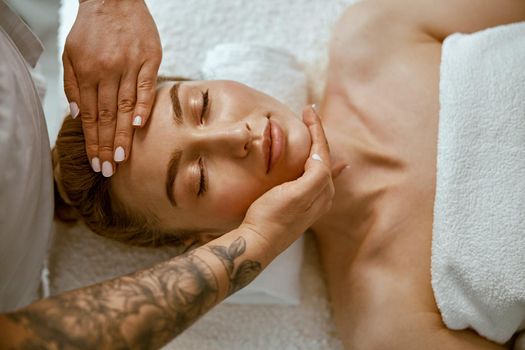 Therapist is doing face relaxing massage to a young woman in modern wellness cabinet