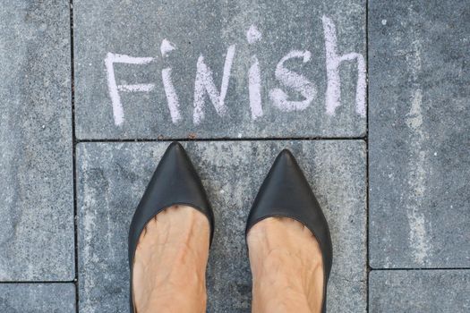 The feet of a woman in black classic shoes before the word finish