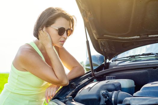 Frustrated woman driver near a broken car. Machine on a country road. The woman has stress