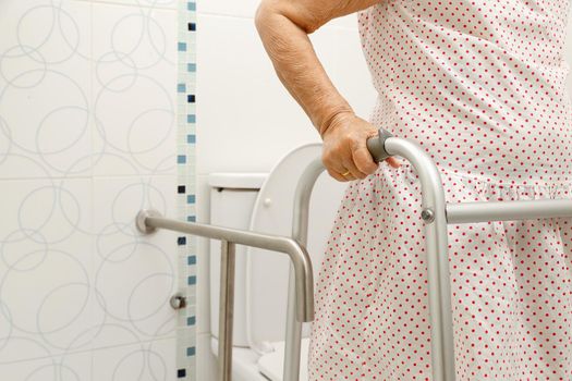 Elderly woman holding on handrail in toilet.