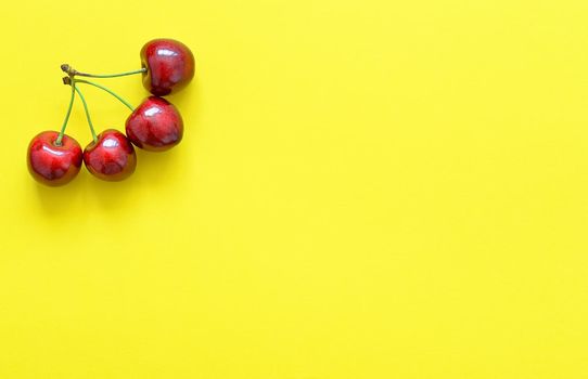 Big sweet cherry isolated on bright yellow background. Summer background. Flat lay, top view. Four red cherries.